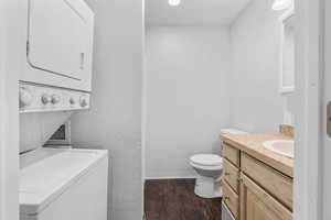 Bathroom featuring a textured wall, toilet, wood finished floors, vanity, and stacked washer and clothes dryer