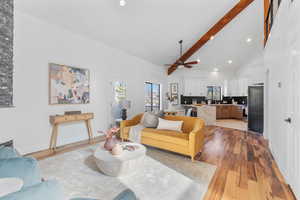 Living area with baseboards, light wood-style flooring, ceiling fan, high vaulted ceiling, and beam ceiling