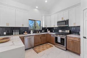 Kitchen with a sink, white cabinetry, marble finish floor, appliances with stainless steel finishes, and backsplash