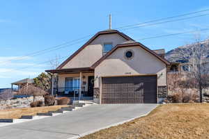 View of front of home with concrete driveway, stone siding, an attached garage, a porch, and stucco siding