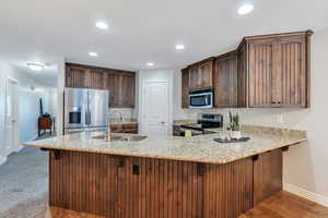 Kitchen with light stone countertops, appliances with stainless steel finishes, a sink, and recessed lighting