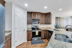 Kitchen with appliances with stainless steel finishes, light stone countertops, light wood-style floors, a sink, and recessed lighting