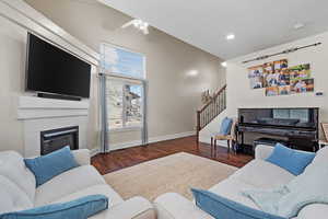 Living room featuring wood finished floors, a ceiling fan, baseboards, stairway, and a tiled fireplace