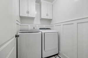 Laundry area featuring wainscoting, cabinet space, independent washer and dryer, and a decorative wall