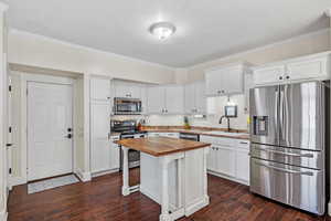 Kitchen featuring dark wood-type flooring, a sink, white cabinetry, wooden counters, and appliances with stainless steel finishes