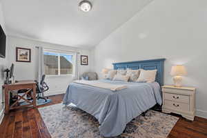 Bedroom with lofted ceiling, dark wood-style flooring, and baseboards