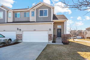 Townhome / multi-family property with a garage, stone siding, concrete driveway, board and batten siding, and a front yard