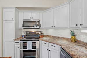 Kitchen with appliances with stainless steel finishes, white cabinetry, and light stone countertops