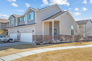 View of front facade with an attached garage, stone siding, concrete driveway, stucco siding, and a front yard