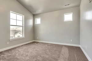 Carpeted spare room with baseboards, visible vents, and vaulted ceiling