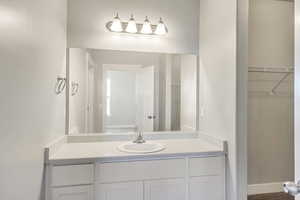 Bathroom featuring baseboards, a walk in closet, and vanity