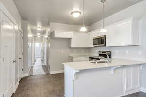 Kitchen featuring dark wood-style floors, appliances with stainless steel finishes, white cabinets, a sink, and a peninsula