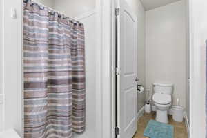 Bathroom featuring baseboards, a shower with shower curtain, toilet, and tile patterned floors