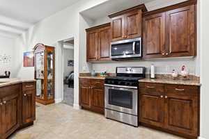 Kitchen with dark brown cabinets, appliances with stainless steel finishes, light tile patterned flooring, and light stone countertops