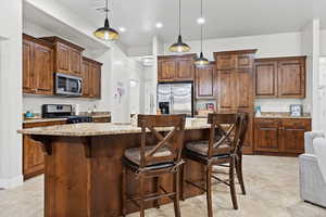 Kitchen featuring light stone counters, appliances with stainless steel finishes, and decorative light fixtures