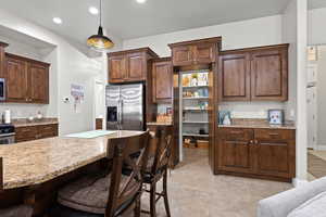 Kitchen with hidden pantry, a breakfast bar area, recessed lighting, stainless steel fridge, and decorative light fixtures