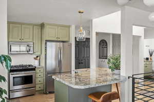 Kitchen with light stone counters, light wood finished floors, stainless steel appliances, cream cabinets, and a kitchen island