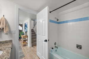 Full bath with washtub / shower combination, vanity, and wood finished floors