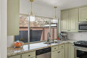 Kitchen with light stone countertops, cream cabinetry, stainless steel appliances, and a sink