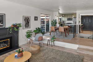 Living area featuring a textured ceiling, a fireplace, baseboards, light wood finished floors, and an inviting chandelier