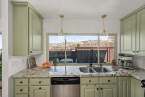 Kitchen with green cabinets, hanging light fixtures, stainless steel dishwasher, and a sink