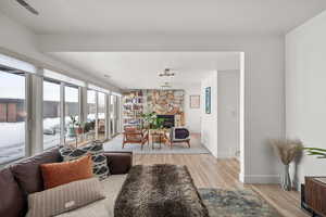 Living area featuring light wood-type flooring, a stone fireplace, and baseboards