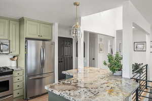 Kitchen featuring appliances with stainless steel finishes, light stone counters, a center island, light wood-type flooring, and green cabinets