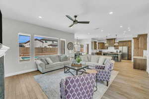 Living room featuring recessed lighting, baseboards, light wood-style flooring, a premium fireplace, and ceiling fan with notable chandelier