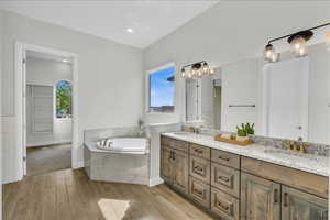 Bathroom with double vanity, a garden tub, a sink, and wood finished floors