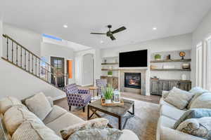 Living room featuring arched walkways, recessed lighting, wood finished floors, stairway, and a glass covered fireplace