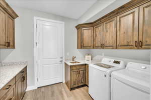 Laundry room with cabinet space, light wood-style flooring, a sink, and washing machine and clothes dryer