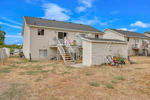 Rear view of property with a deck, fence, stairway, a yard, and a shingled roof