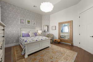 Bedroom featuring wood finished floors, a notable chandelier, baseboards, and wallpapered walls