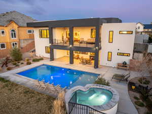 Back of house with a balcony, an in ground hot tub, stucco siding, and a patio