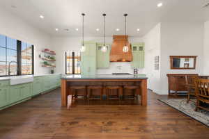 Kitchen featuring custom range hood, a kitchen island, a sink, green cabinets, and a wealth of natural light