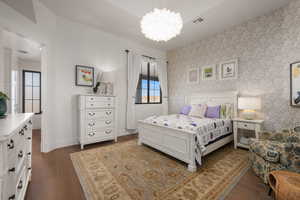 Bedroom with a notable chandelier, visible vents, baseboards, dark wood-style floors, and wallpapered walls