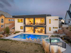 Back of house with a balcony, stucco siding, a pool with connected hot tub, and a patio