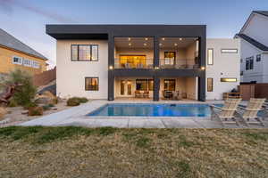 Back of property with an outdoor pool, a patio area, a balcony, and stucco siding