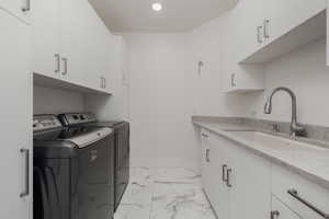 Laundry room with cabinet space, baseboards, marble finish floor, separate washer and dryer, and a sink