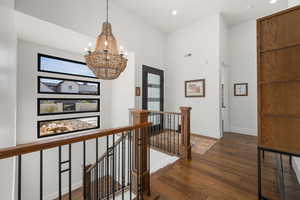 Hall with a notable chandelier, visible vents, hardwood / wood-style floors, an upstairs landing, and baseboards