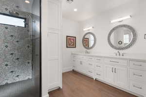 Full bath featuring double vanity, wood finished floors, walk in shower, and a sink