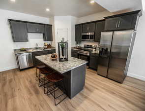 Kitchen with a center island, light wood finished floors, stainless steel appliances, light stone countertops, and a kitchen bar