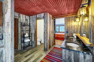 Ensuite bathroom with toilet, wooden walls, wood finished floors, wood ceiling, and a sink