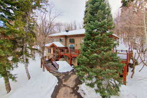 Snow covered back of property featuring stairs, stone siding, and a wooden deck