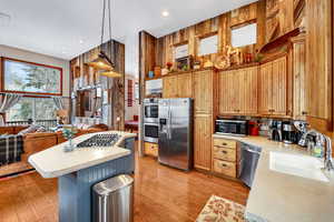 Kitchen featuring light wood-style flooring, a kitchen island, appliances with stainless steel finishes, light countertops, and a sink