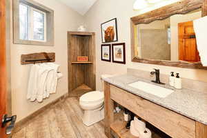 Bathroom featuring baseboards, tiled shower, toilet, wood finished floors, and vanity