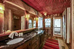 Bathroom featuring wood walls, wood ceiling, a sink, and wood finished floors