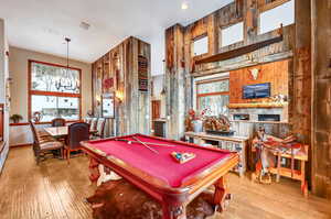 Game room with a chandelier, billiards, a stone fireplace, and hardwood / wood-style flooring