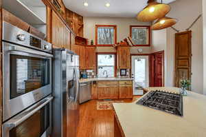 Kitchen featuring a sink, a towering ceiling, light countertops, appliances with stainless steel finishes, and light wood finished floors