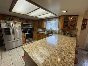 Kitchen featuring light tile patterned floors, a peninsula, a sink, appliances with stainless steel finishes, and tasteful backsplash